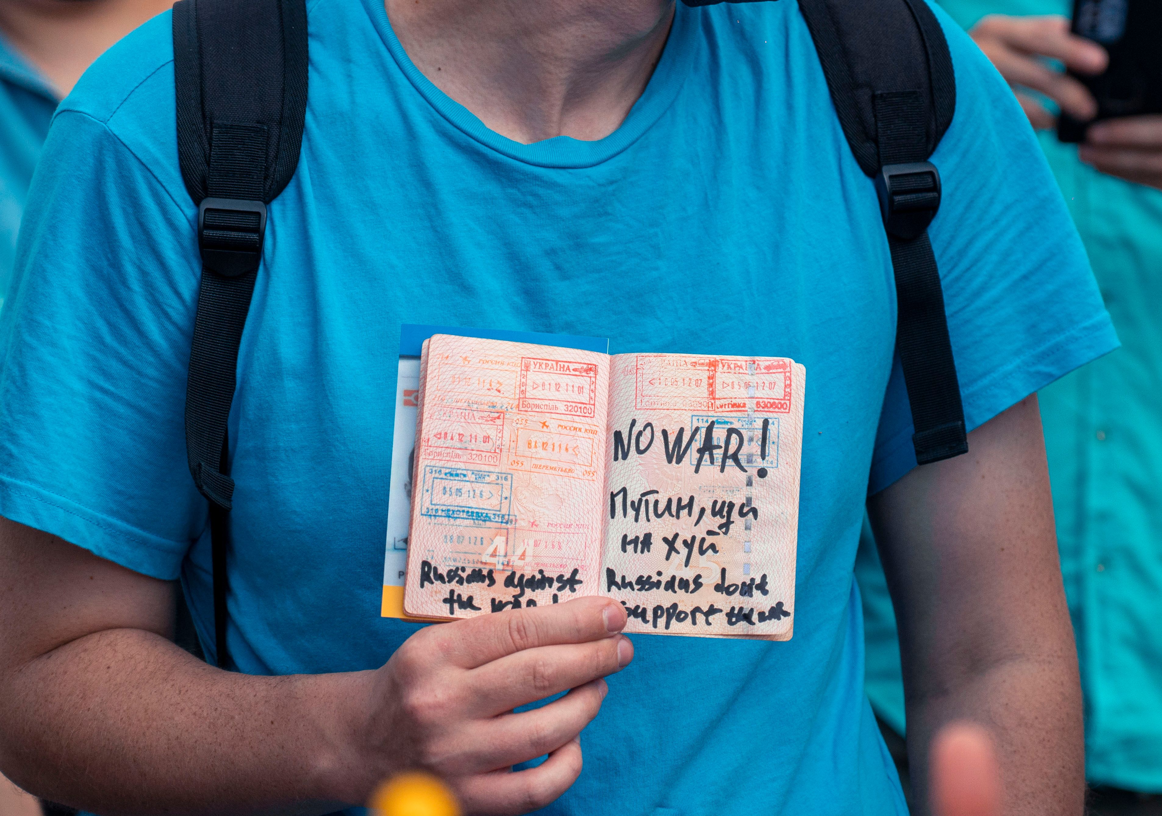 A person in a blue shirt holds a passport featuring anti-war messages.
