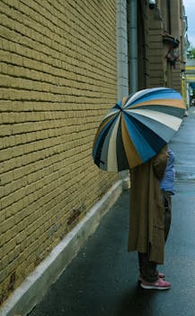 Woman holding a colorful umbrella on a rainy day in Moscow, Russia, standing by a brick wall.