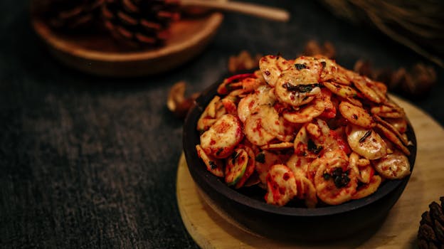 Close-up of a spicy fried snack served in a rustic wooden bowl on a dark background.