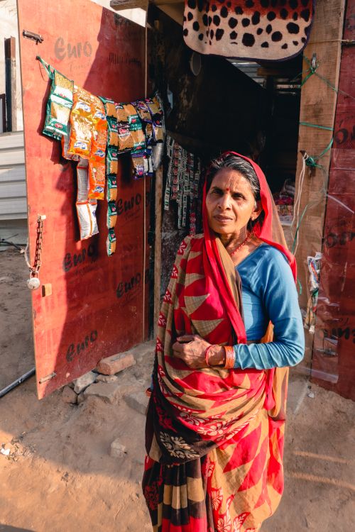 Free Elderly Indian woman wearing traditional attire stands outside a shop in a rural setting. Stock Photo