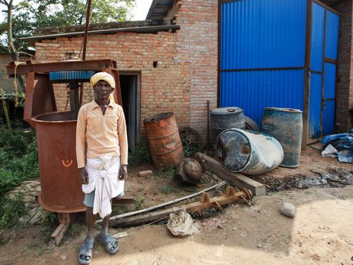 Free A man stands beside industrial barrels in a rural setting with brick buildings. Stock Photo