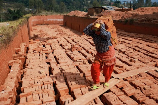 A person balances a stack of bricks in an outdoor brick factory, demonstrating traditional labor methods.