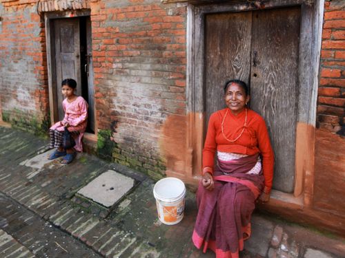 Free Woman and child sitting in front of wooden doors in a rustic, brick walled setting. Stock Photo