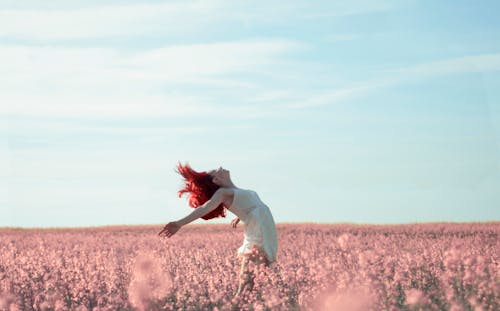 Женщина в желтом платье стоит на поле с розовыми лепестками цветов