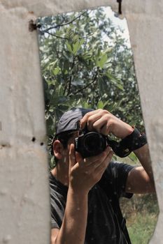 A photographer captures his reflection in a jagged mirror amid lush greenery, creating a unique self-portrait.