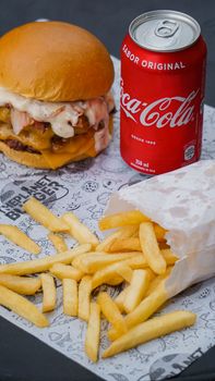 Appetizing burger meal with cheese, fries, and a can of Coca-Cola on textured paper.