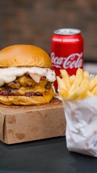 Delicious cheeseburger and fries with a can of Coca-Cola on the side, perfect for fast food lovers.