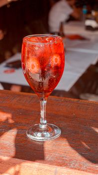 Close-up of a vibrant red cocktail with ice in a glass on a wooden table.