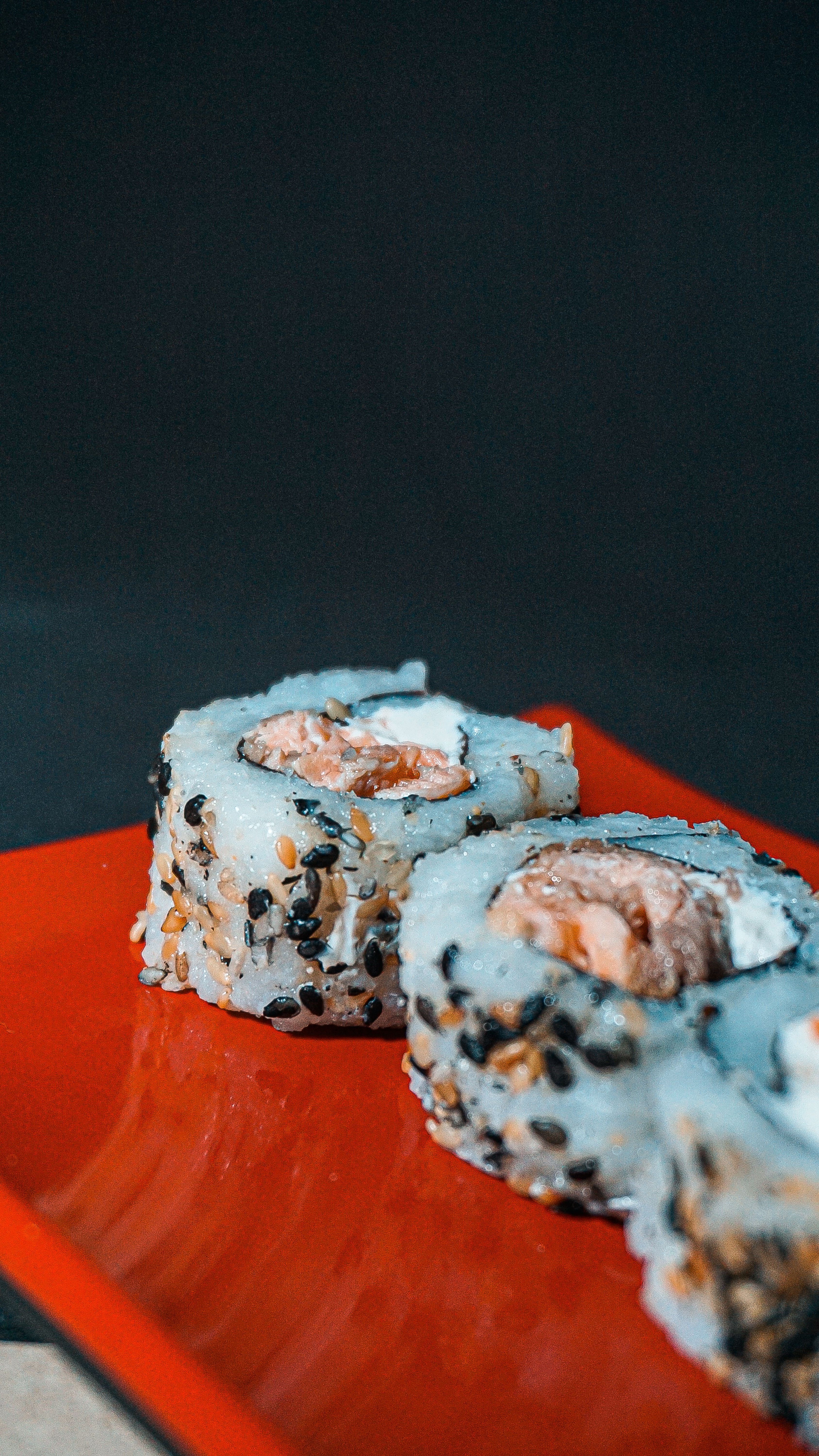 Close-up of sushi rolls with sesame seeds on a red plate, showcasing Japanese cuisine.