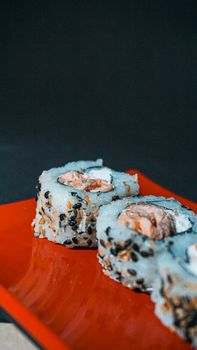 Close-up of sushi rolls with sesame seeds on a red plate, showcasing Japanese cuisine.