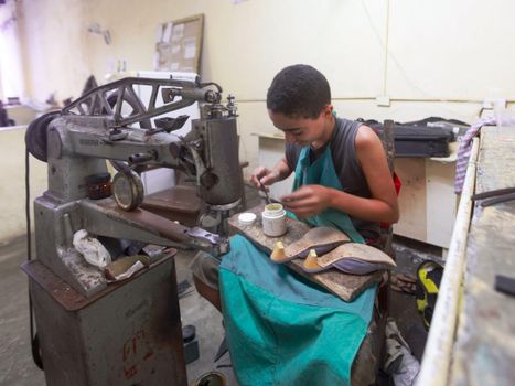 A young shoe repairer focuses intently on his work, surrounded by tools and machinery.