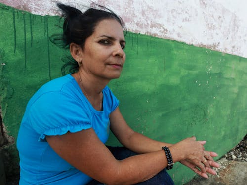 Woman in Blue Shirt Sitting Beside a Green Wall