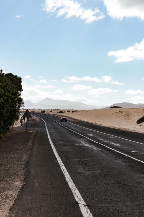 Empty highway stretching through open desert under a blue sky with scattered clouds