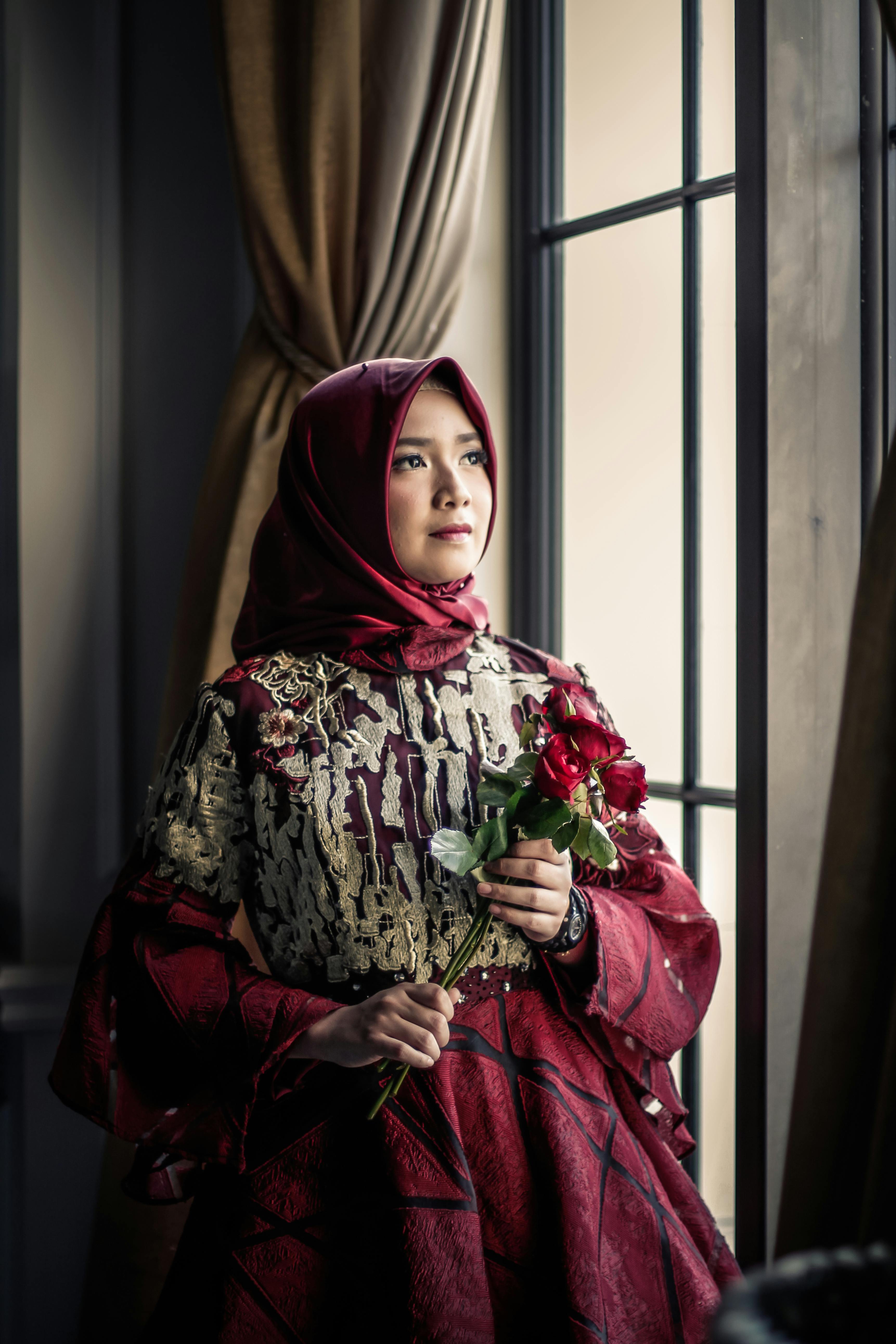 一位戴着玫瑰头巾、身着优雅传统服装的时尚女士在窗前摆着姿势