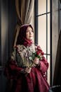 一位戴着玫瑰头巾、身着优雅传统服装的时尚女士在窗前摆着姿势
