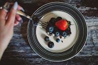 木桌上放着一个优雅的甜点盘，盘中有巧克力蛋糕、蓝莓和草莓，旁边配有一把叉子