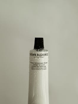Close-up of a Grown Alchemist Hydra-Repair Day Cream tube with droplets, minimalist style.