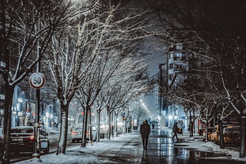 Free Urban winter scene of people walking on a snowy city street at night, illuminated by streetlights. Stock Photo