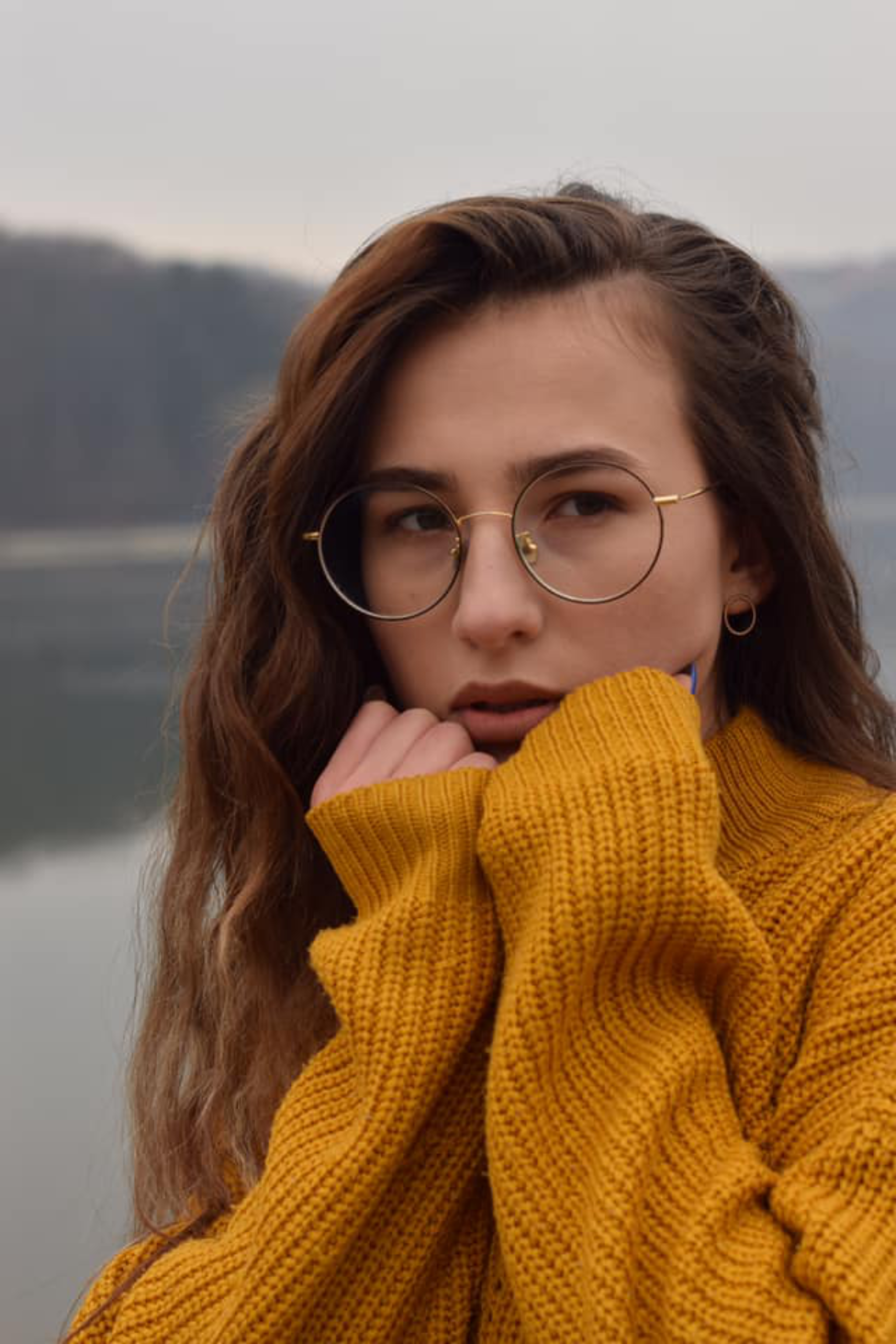 Woman in a cozy yellow sweater by a lake, exuding warmth and contemplation.
