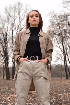 A confident woman stands with hands in pockets in a serene autumn park setting.