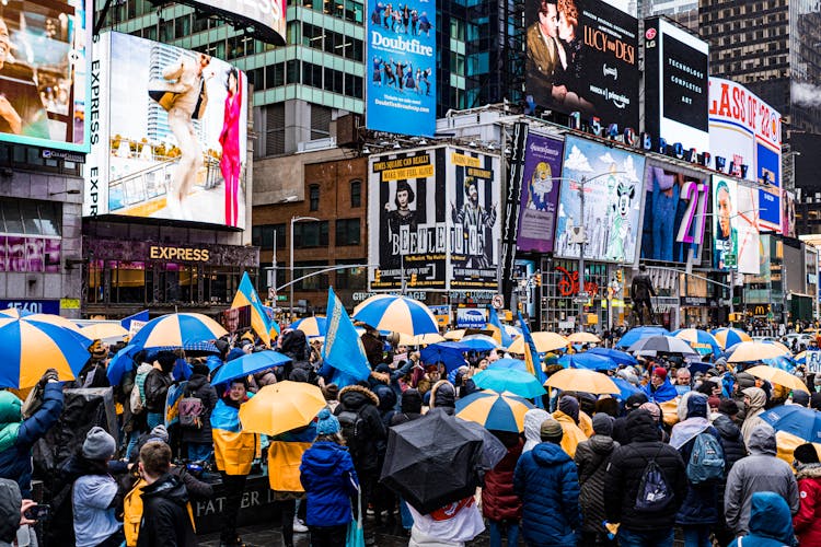 A Crowd With Umbrellas Near Buildings With Billboards