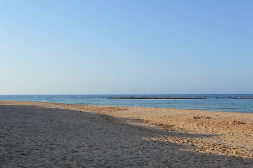 Free A tranquil sandy beach meets the clear blue sea under a bright sky. Stock Photo