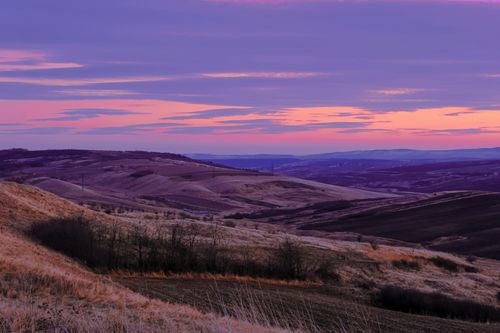Free A stunning sunrise paints the sky over rolling hills with serene hues of purple and pink. Stock Photo