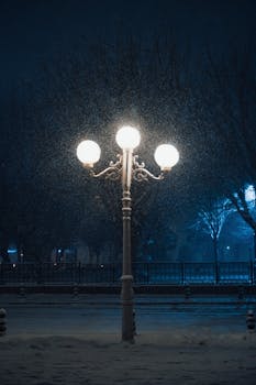 A tranquil snowy evening scene with a glowing street lamp casting light amidst gentle snowfall.