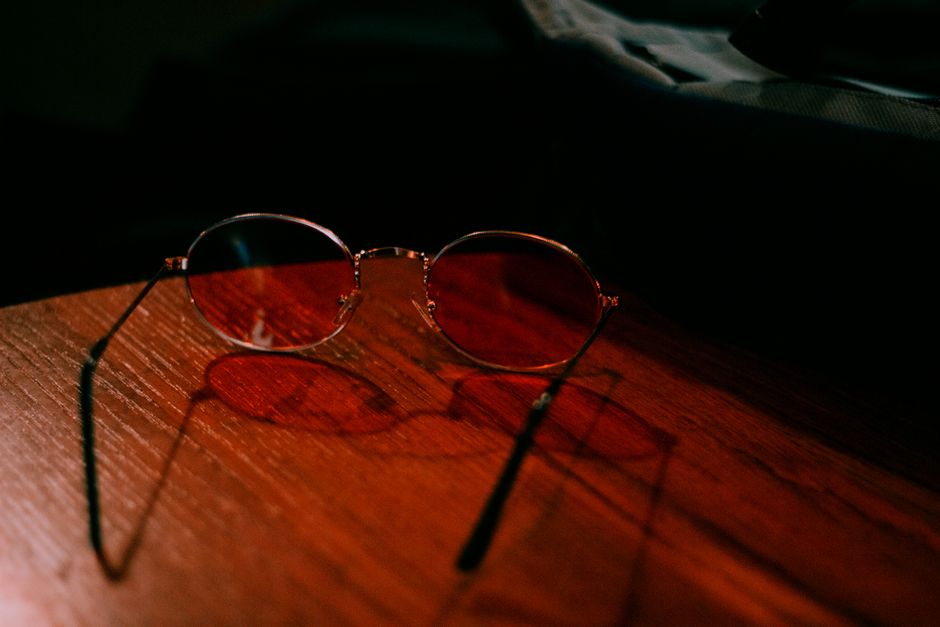 Artistic shot of round eyeglasses on a wooden table, casting shadows.