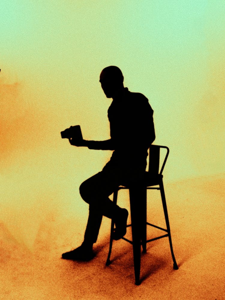 Silhouette Of Man Sitting On Chair Holding A Thing
