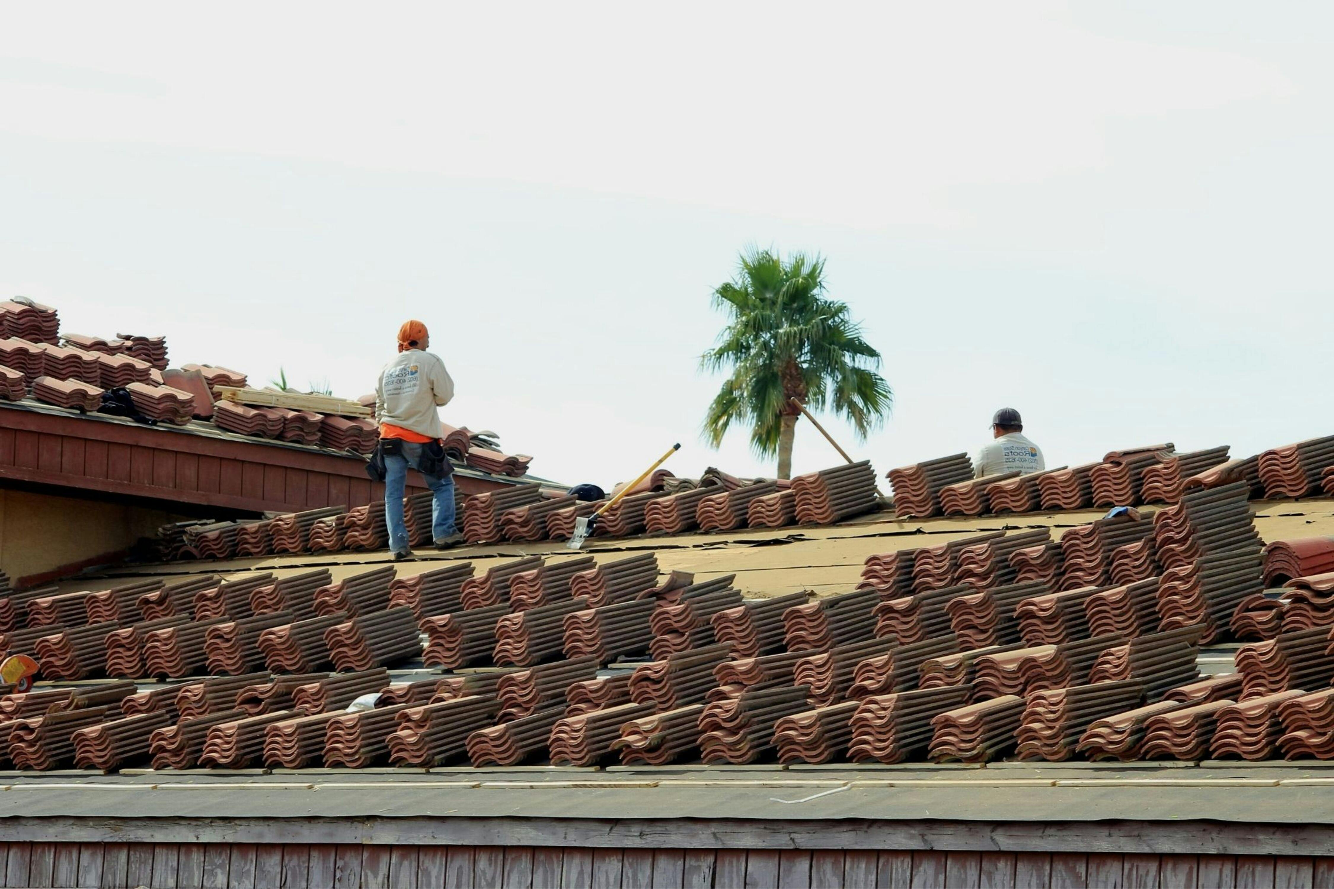 Construction workers installing terra cotta roof tiles under the sunny Phoenix sky.