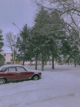A classic red car parked in a serene snowy landscape, surrounded by trees.