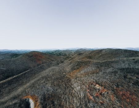 Drone shot of a tranquil mountain range with winding road and dense forest.