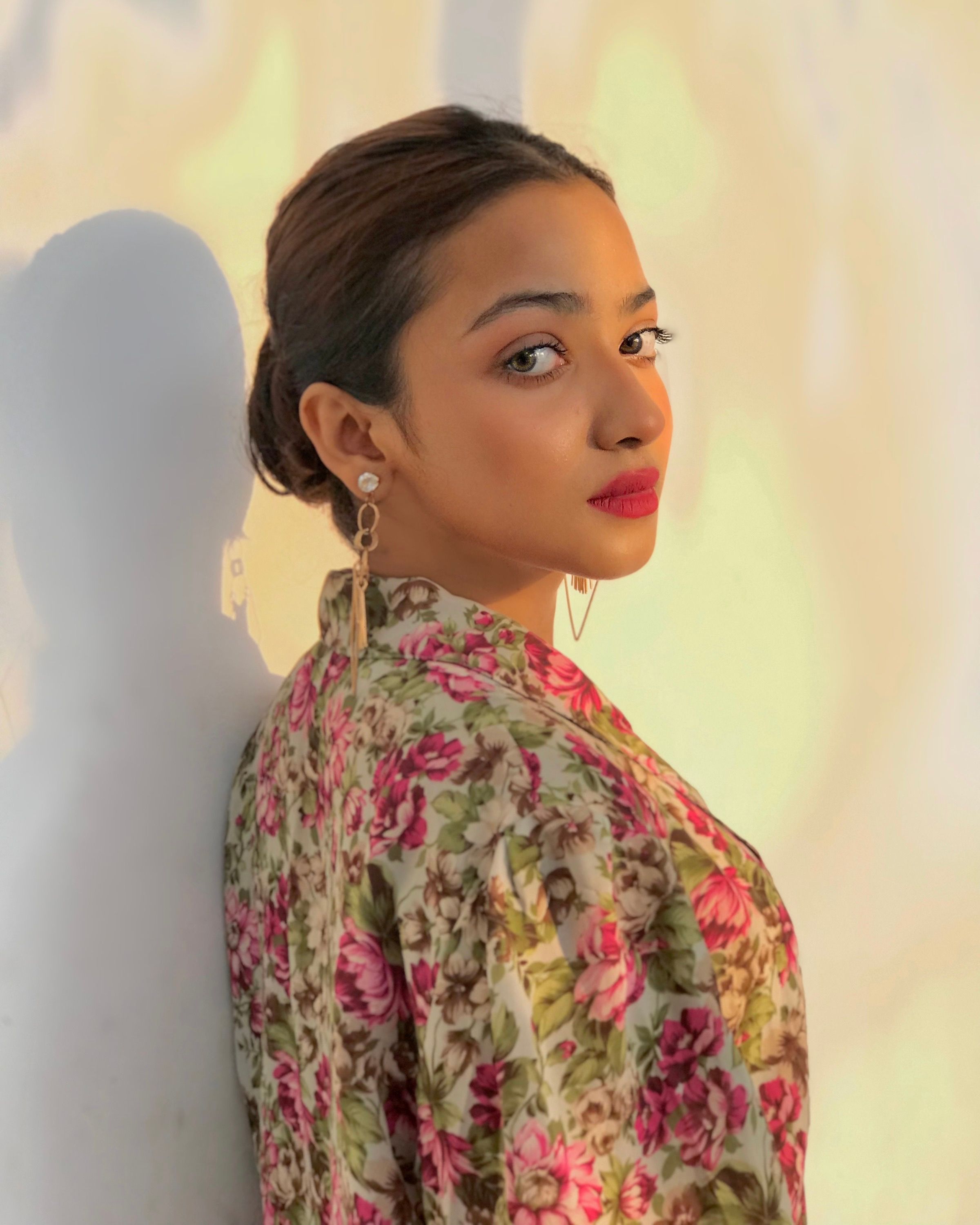 A woman in a floral top poses confidently, showing elegance and style in the soft lighting.