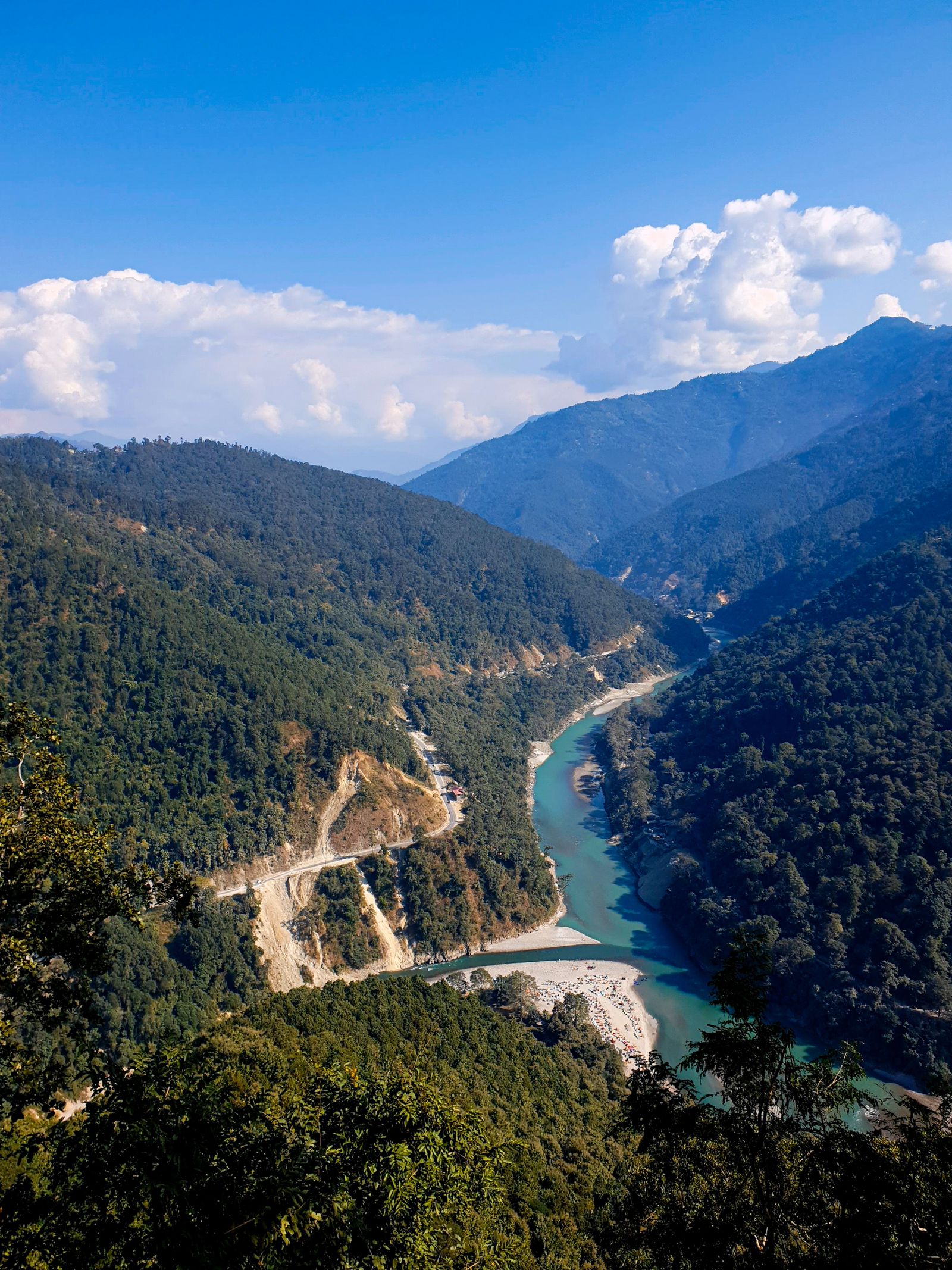 The jade Teesta curving between steep forested hills in the Darjeeling district, a highway beside it