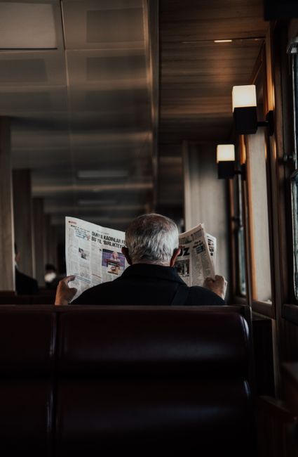 A senior man reads a newspaper while traveling on a train, creating a cozy and introspective mood.