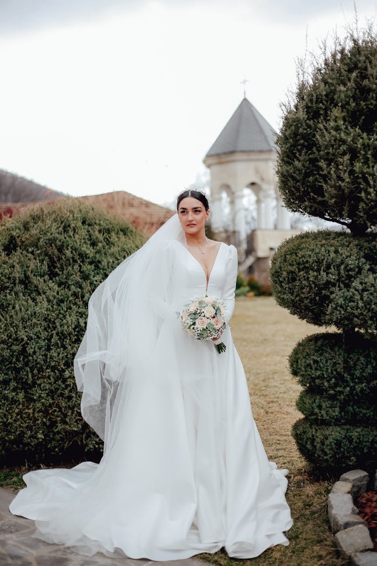 Bride In White Long Dress And Veil With Bunch Of Flowers In Hand