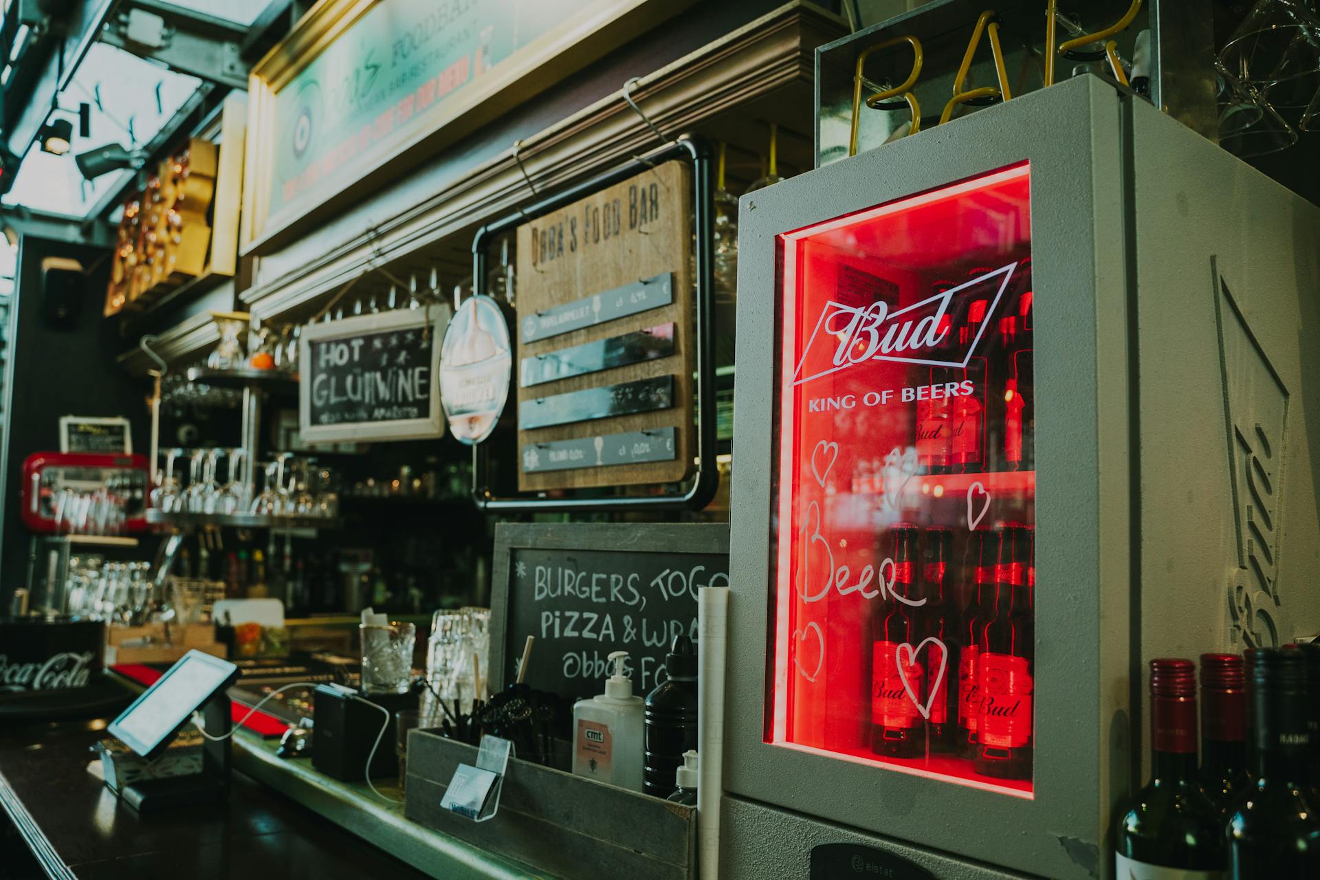 Inviting pub interior featuring illuminated beer fridge, drink options and rustic decor.