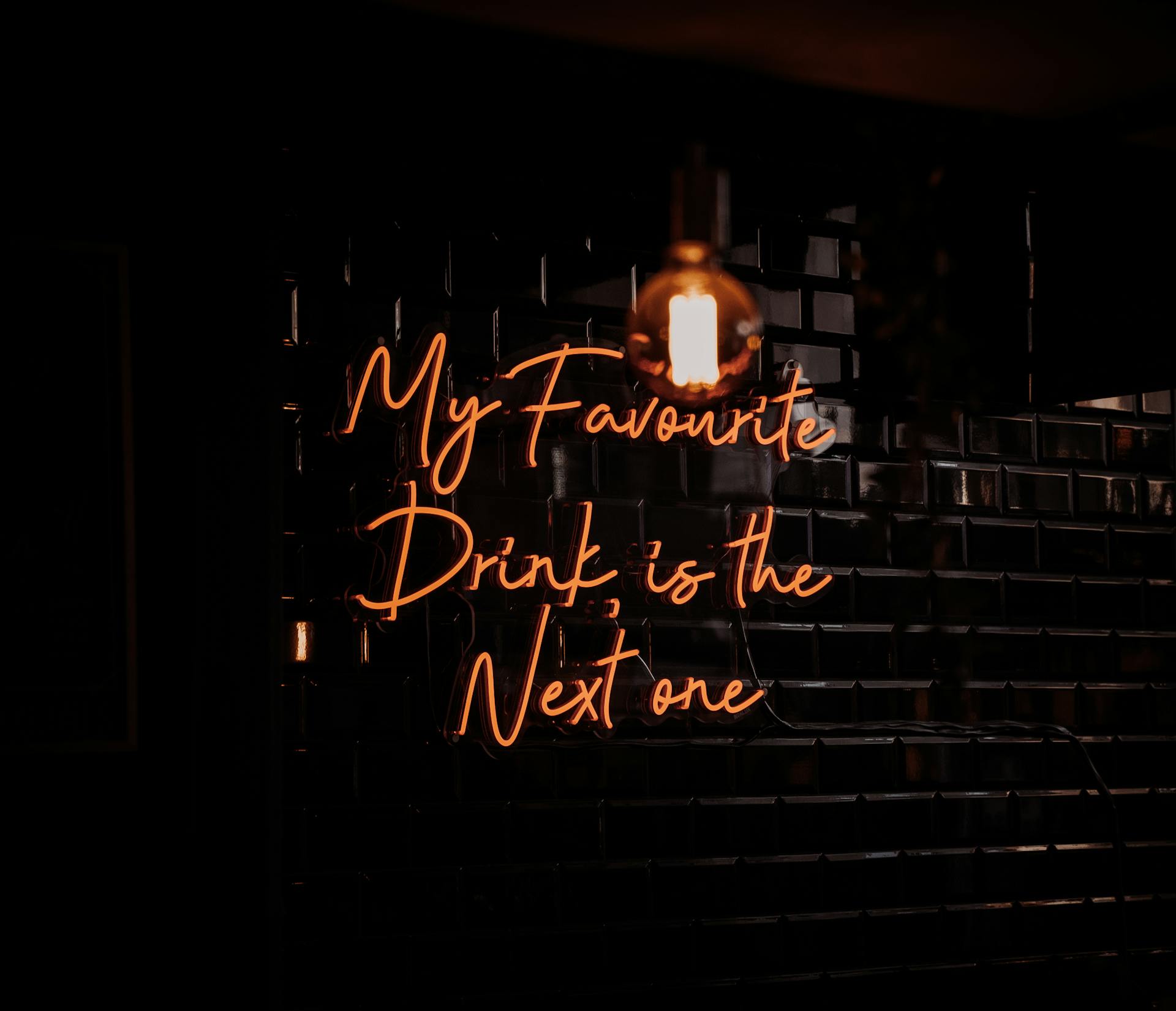 Moody shot of a neon bar sign reading 'My Favourite Drink is the Next One'.