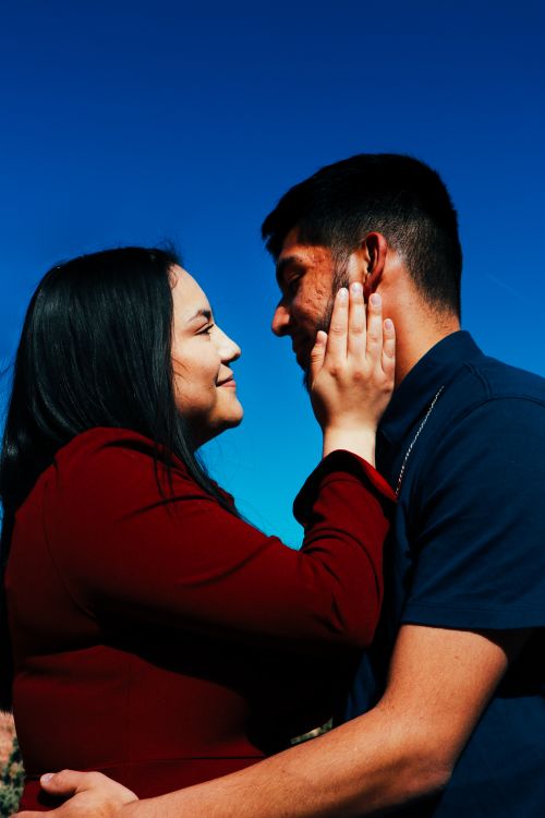 Free A couple sharing a tender moment outdoors under a clear blue sky. Captures the essence of love and affection. Stock Photo