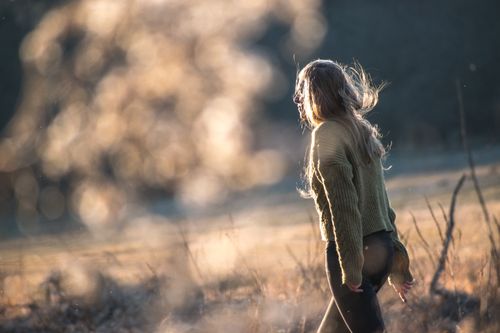 Free A woman in a sweater walks through a sunlit field, capturing the essence of freedom and nature. Stock Photo