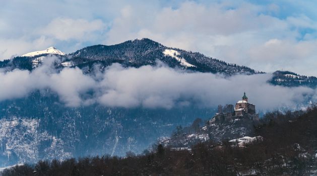 Scenic view of Castel Ivano amidst snowy mountains and clouds in Trentino, Italy.