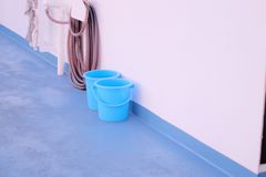A minimalist composition of two blue buckets against a white wall with a hose nearby.