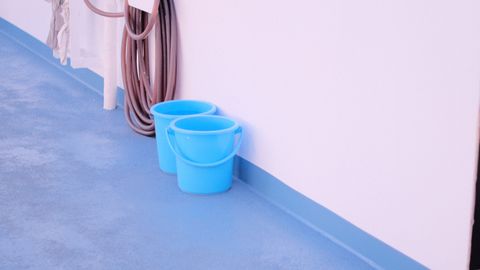 A minimalist composition of two blue buckets against a white wall with a hose nearby.