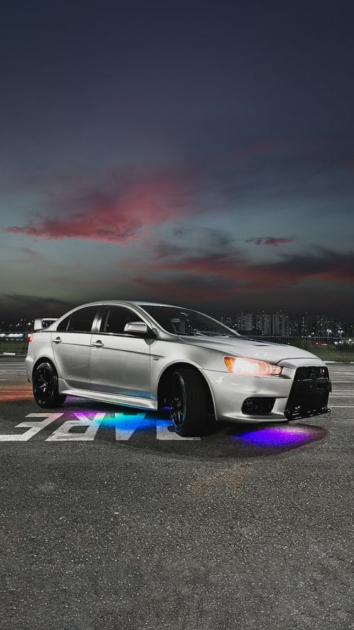 Free Silver sports car with colorful underglow parked against city skyline at twilight. Stock Photo