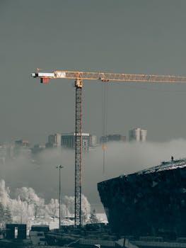 A tower crane stands tall amidst a foggy winter cityscape with modern architecture in Novosibirsk, Russia.
