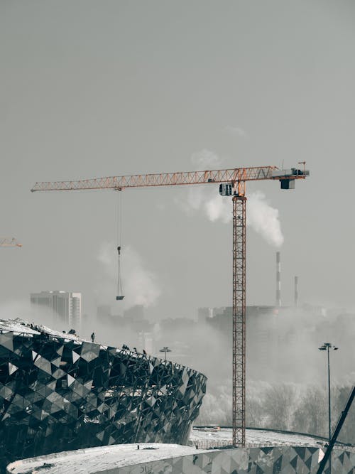 елтый башенный кран на строительной ощадке ледовой арены в тумане