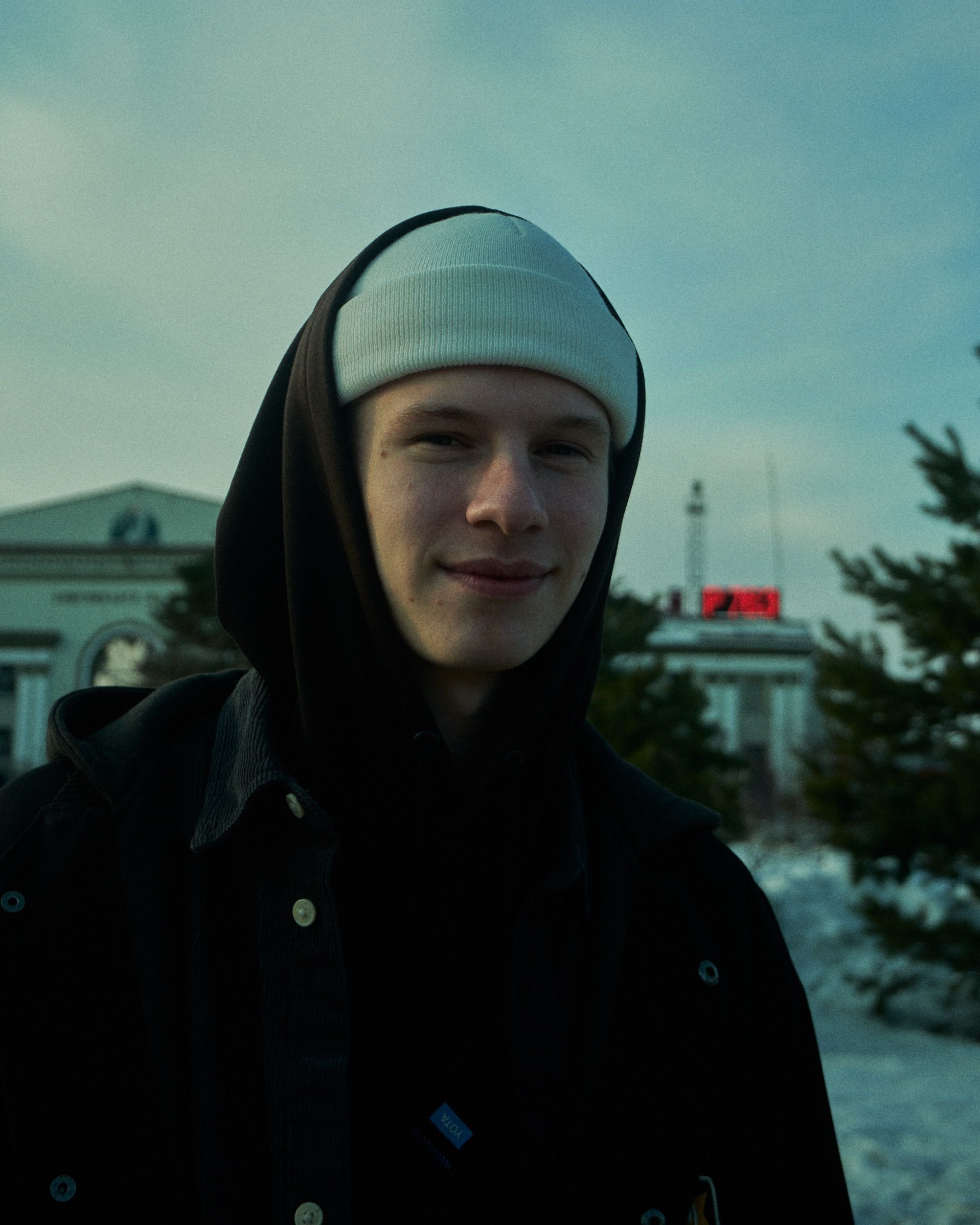 Smiling young man wearing a hoodie and beanie in a winter setting outdoors.