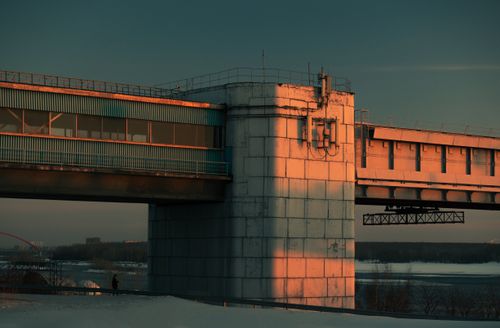Free A concrete bridge spans over a snowy river under the warm glow of sunset in winter. Stock Photo