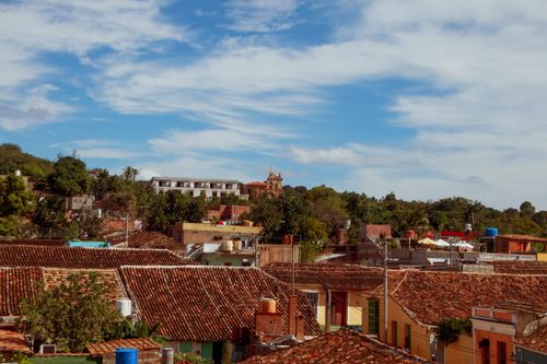 Free A scenic view of colonial rooftops and lush greenery under a vibrant blue sky with white clouds. Stock Photo